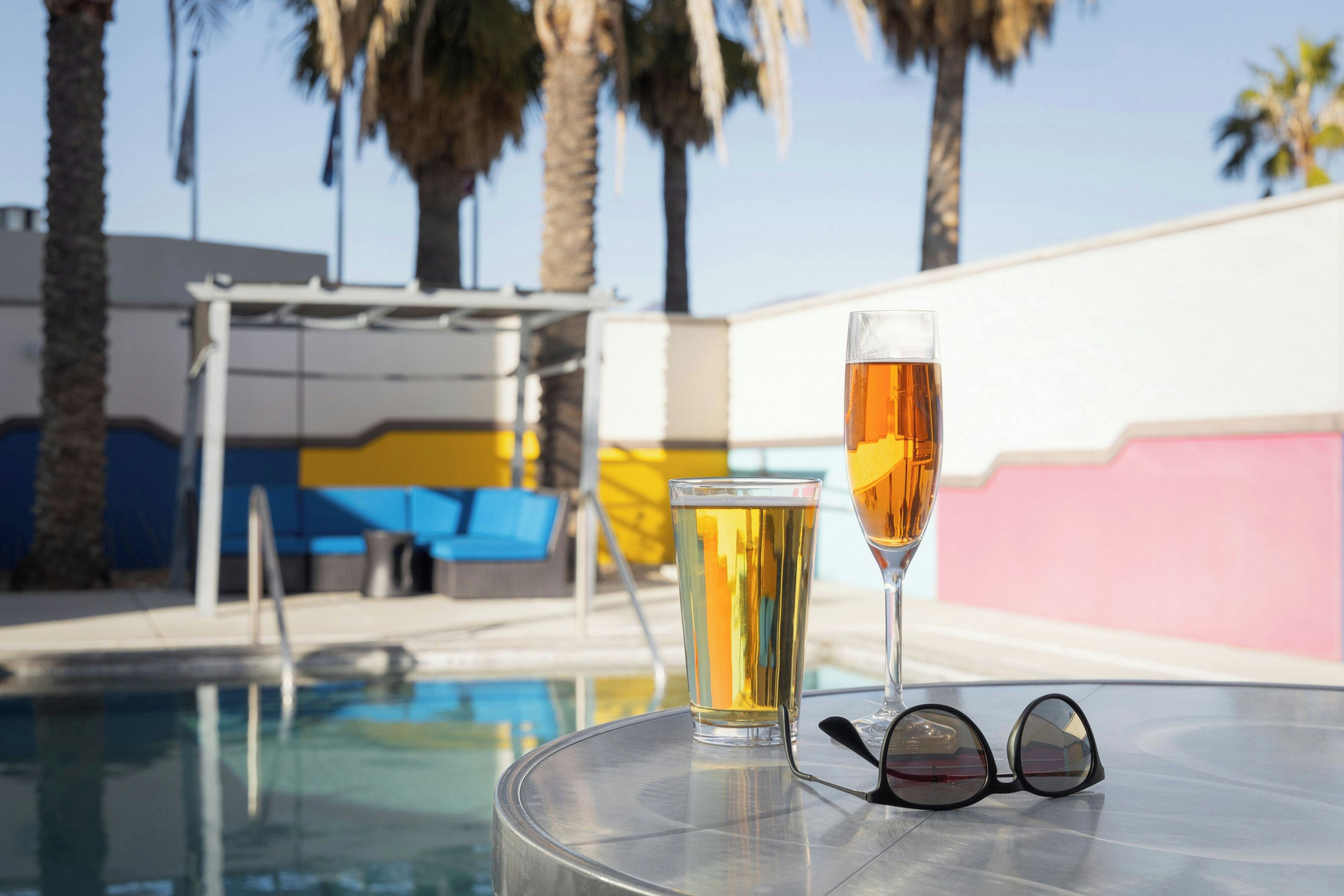 A glass table with two glasses of beer and a pair of sunglasses.