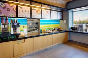 A modern coffee station with a menu board, coffee machines, and a trash bin.