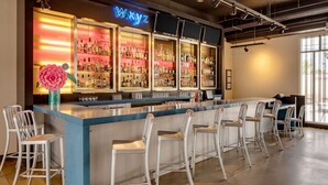 A bar area with a blue counter, white bar stools, and shelves of liquor bottles. - Aloft by Marriott Tucson University (Tucson)