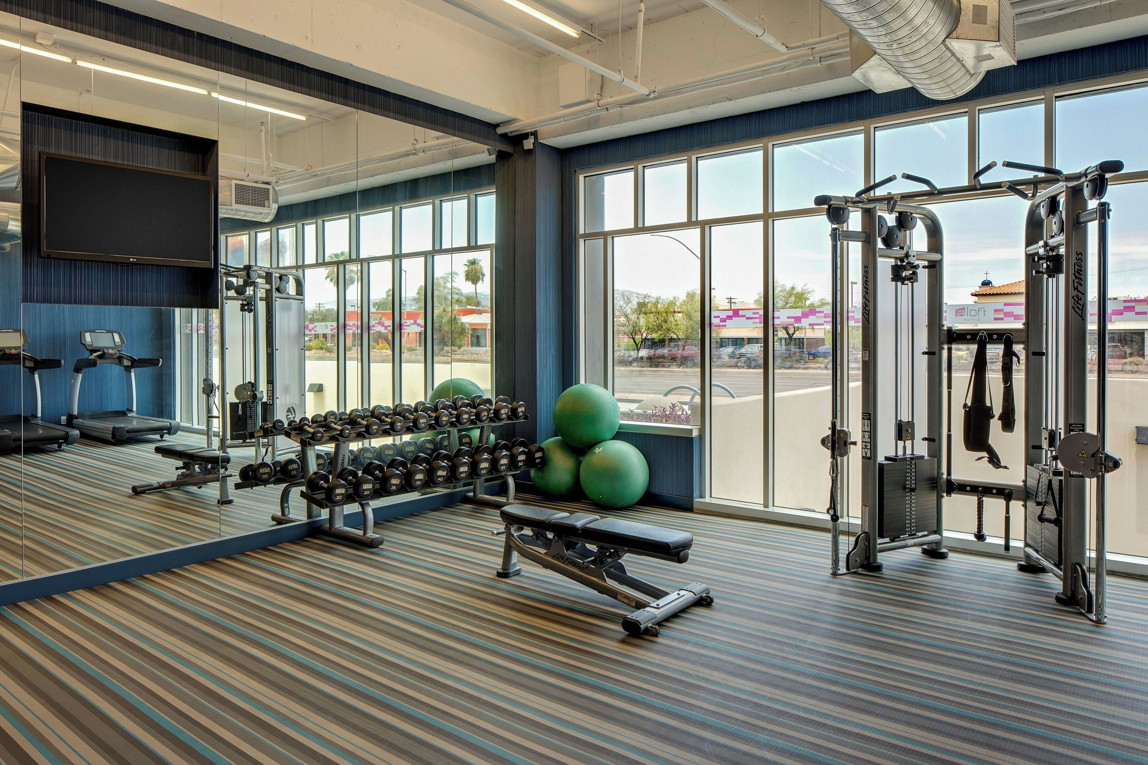 Une salle de sport équipée de matériel d’exercice, d’un banc, d’haltères et dotée de grandes fenêtres.