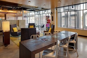 A modern office space with a glass-top table, white chairs, and a sofa with yellow cushions.