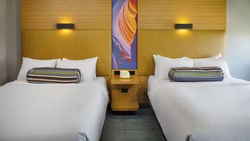 Habitación de hotel con dos camas, cada una con un cojín a rayas y una mesita de noche con un reloj.
