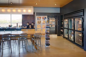 Een modern café met een houten tafel en metalen stoelen, een drankendisplay en een koelkast met glazen deuren.