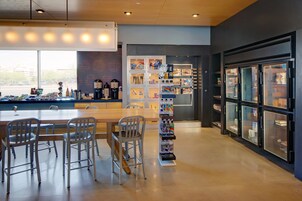 A modern cafe with a wooden table and metal chairs, a beverage display, and a refrigerator with glass doors.
