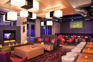 A modern lounge area with a fireplace, comfortable seating, and a large screen displaying a sports event.