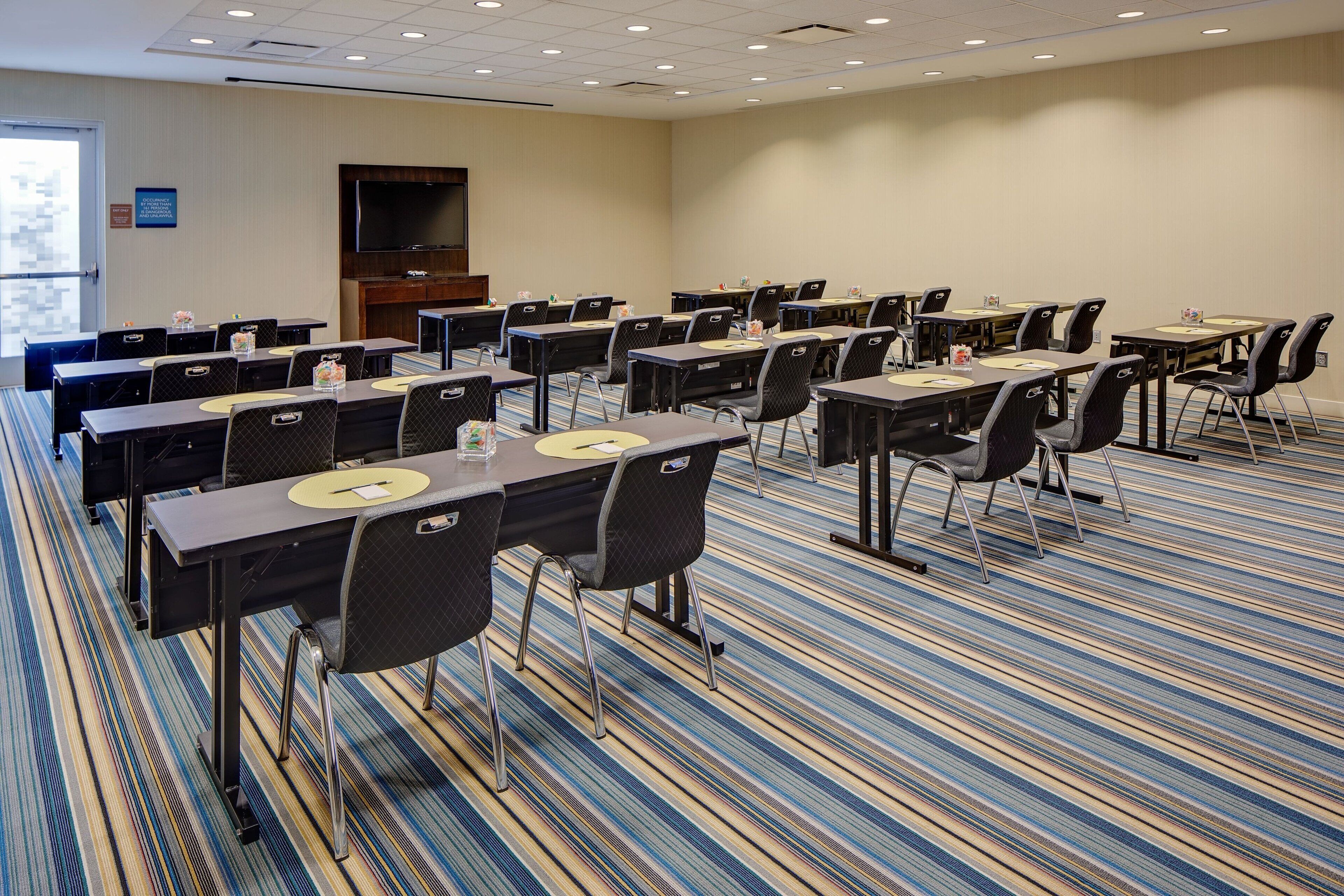 Un salón de conferencias con varias mesas y sillas, un televisor de pantalla plana y piso alfombrado.