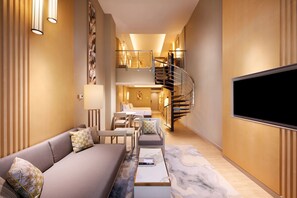 Una sala de estar moderna con un sofá, una mesa de centro y un televisor. Una escalera conduce a un nivel superior con un comedor.