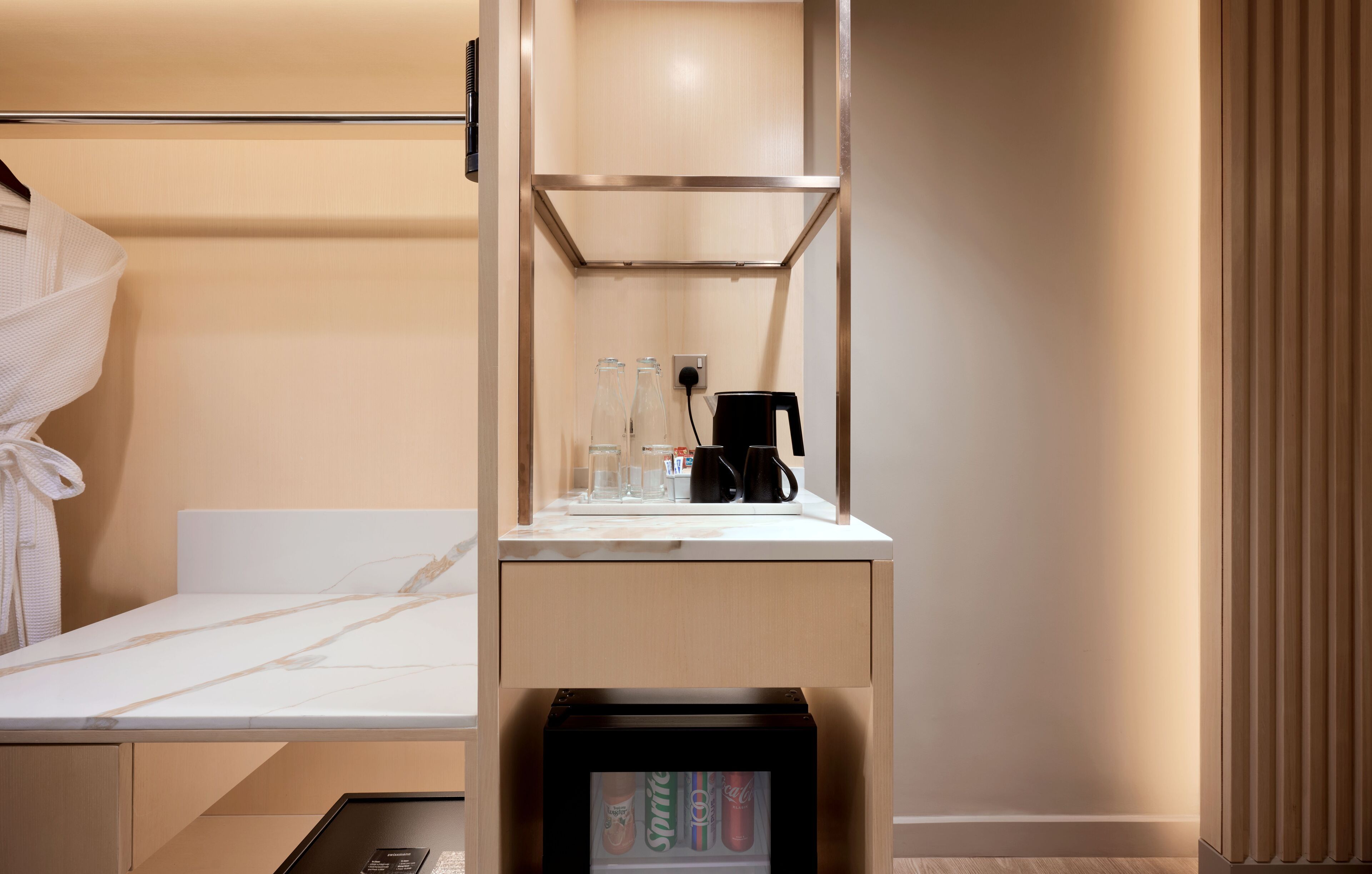 Una habitación de hotel con una cama, un minibar, una cafetera y una botella de Sprite.
