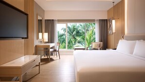 A hotel room with a bed, desk, chair, TV, and a large window with a view of palm trees.