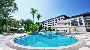 A swimming pool with a surrounding tiled deck, palm trees, and a building with multiple windows.