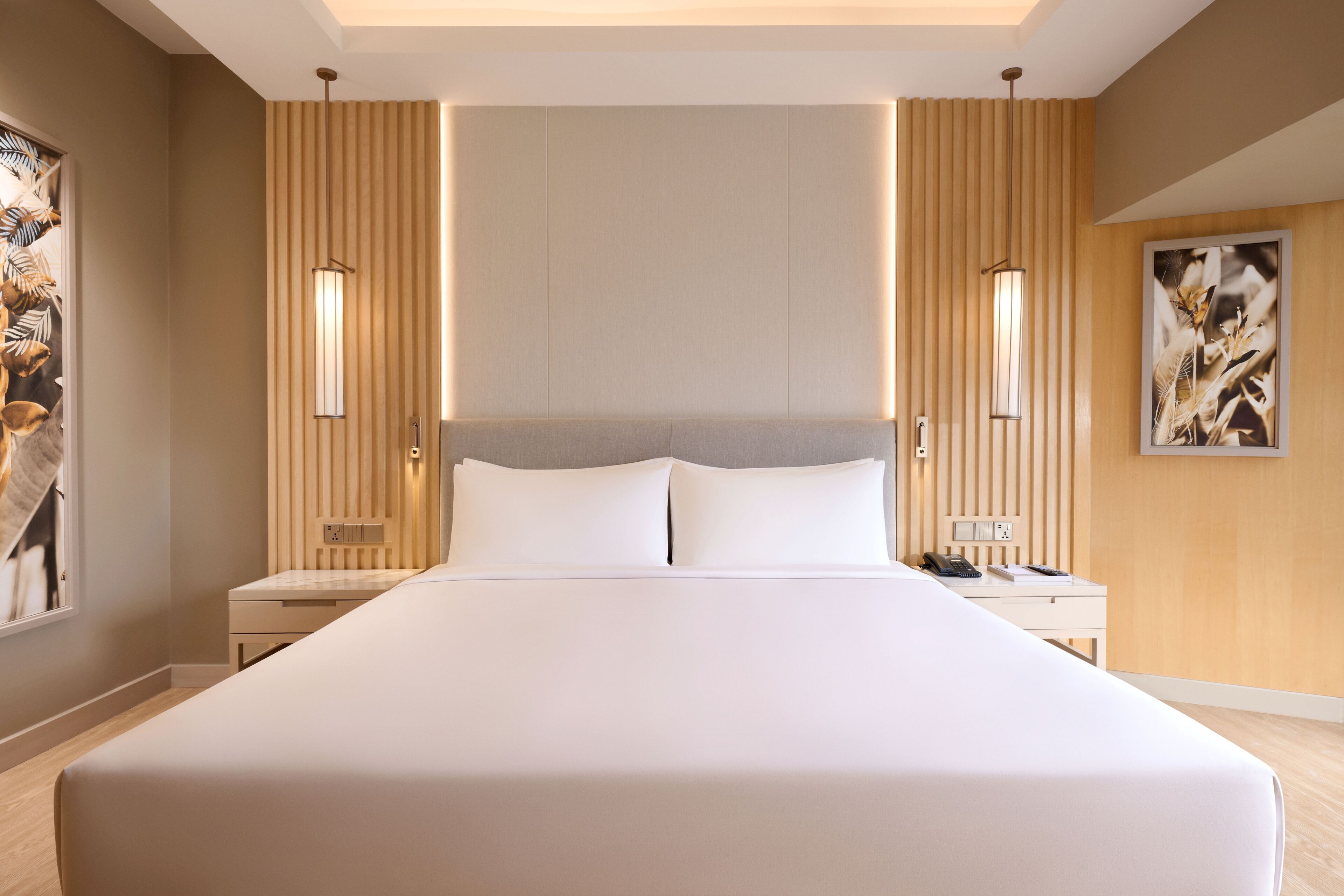 A modern hotel room with a large bed, two bedside tables, a nightstand, a wall-mounted lamp, and a framed picture.