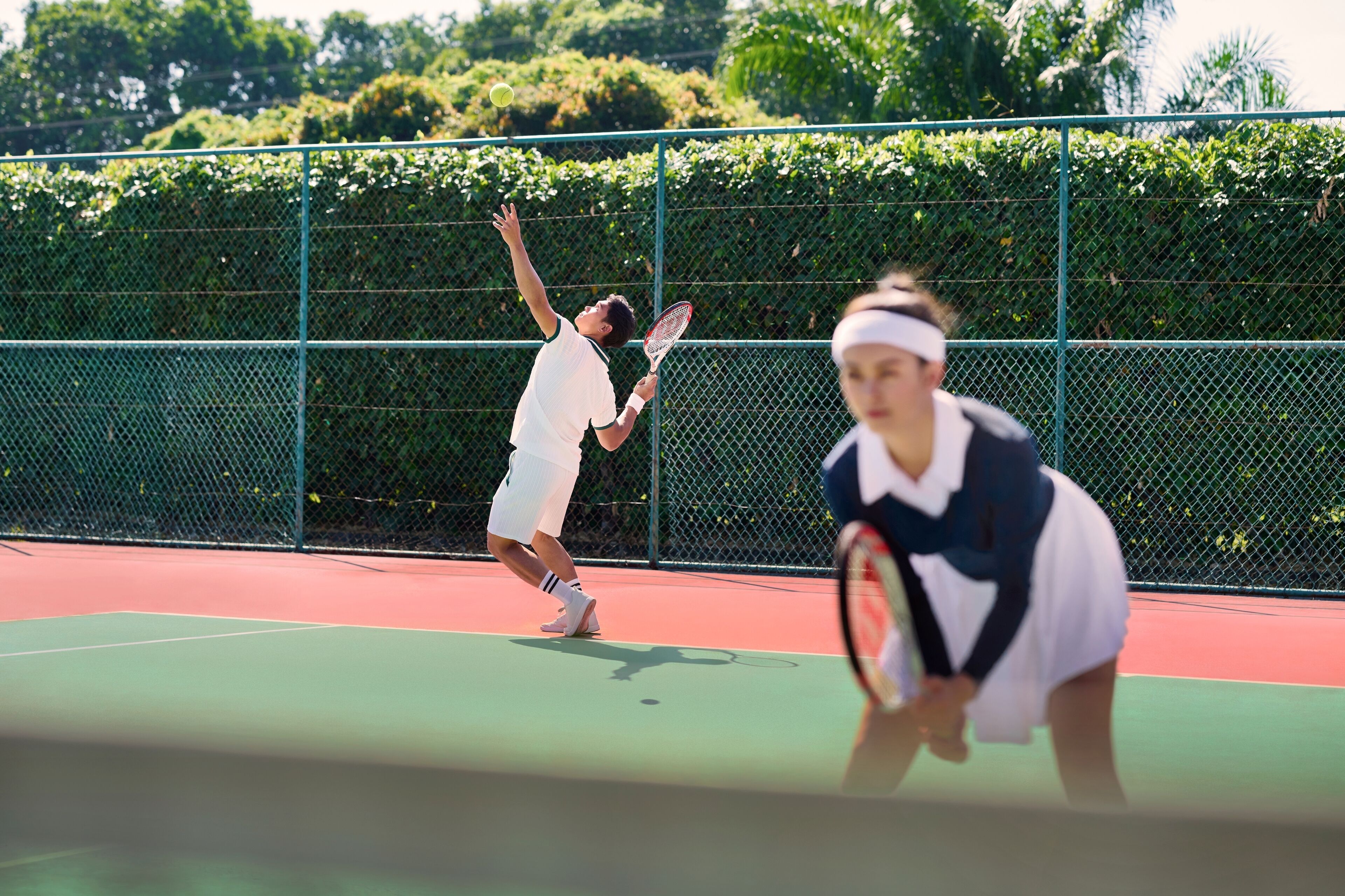 Ein Tennisplatz mit grünem Zaun und Bäumen im Hintergrund.