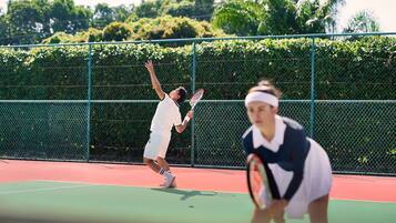 A tennis court with a green fence and trees in the background.