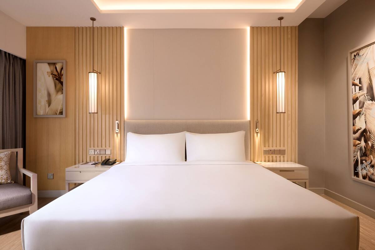 Une chambre d’hôtel avec un grand lit, des tables de chevet, une chaise et des œuvres d’art accrochées aux murs.