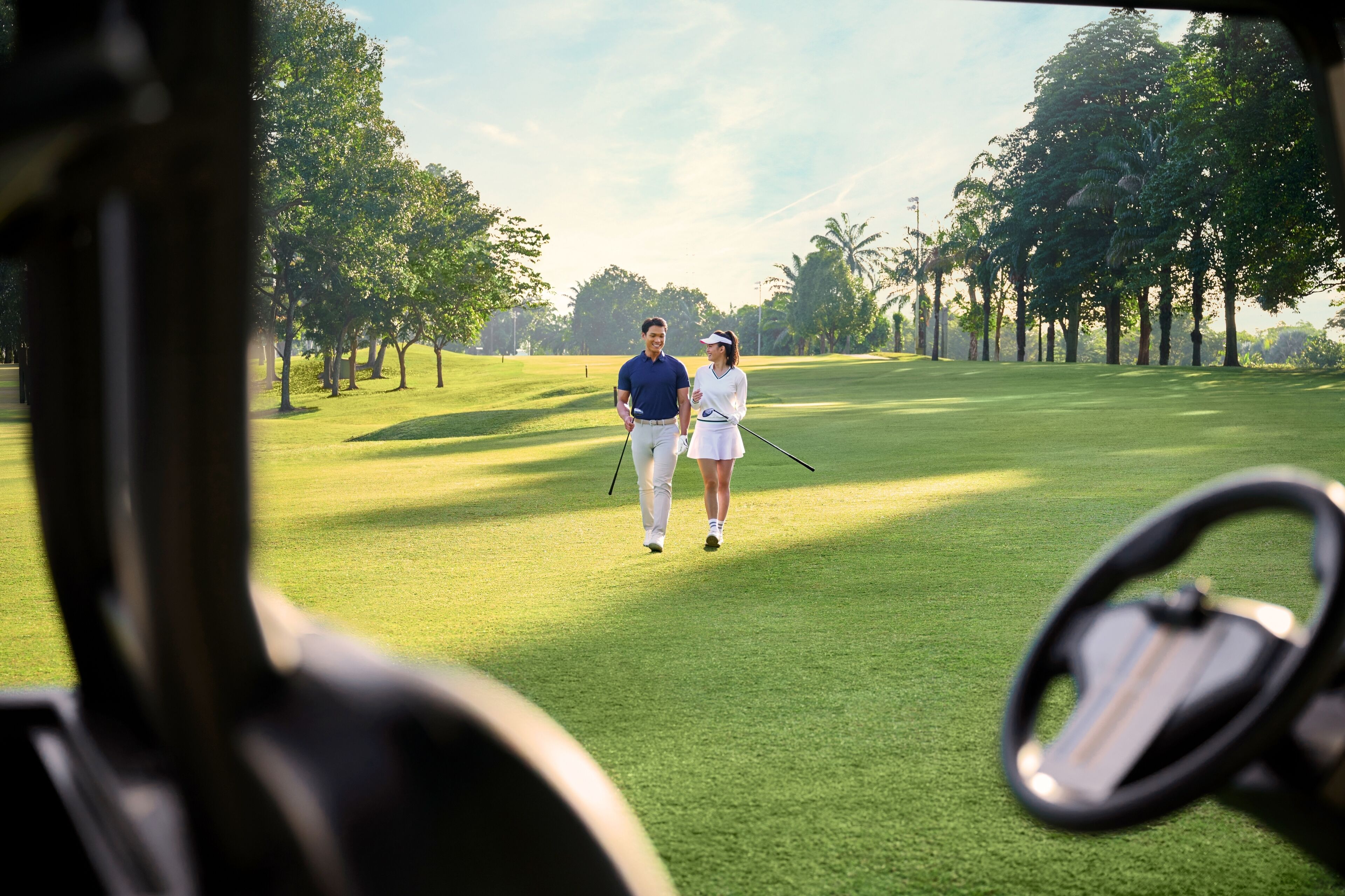 A golf course with a clear path, trees, and a golf cart.