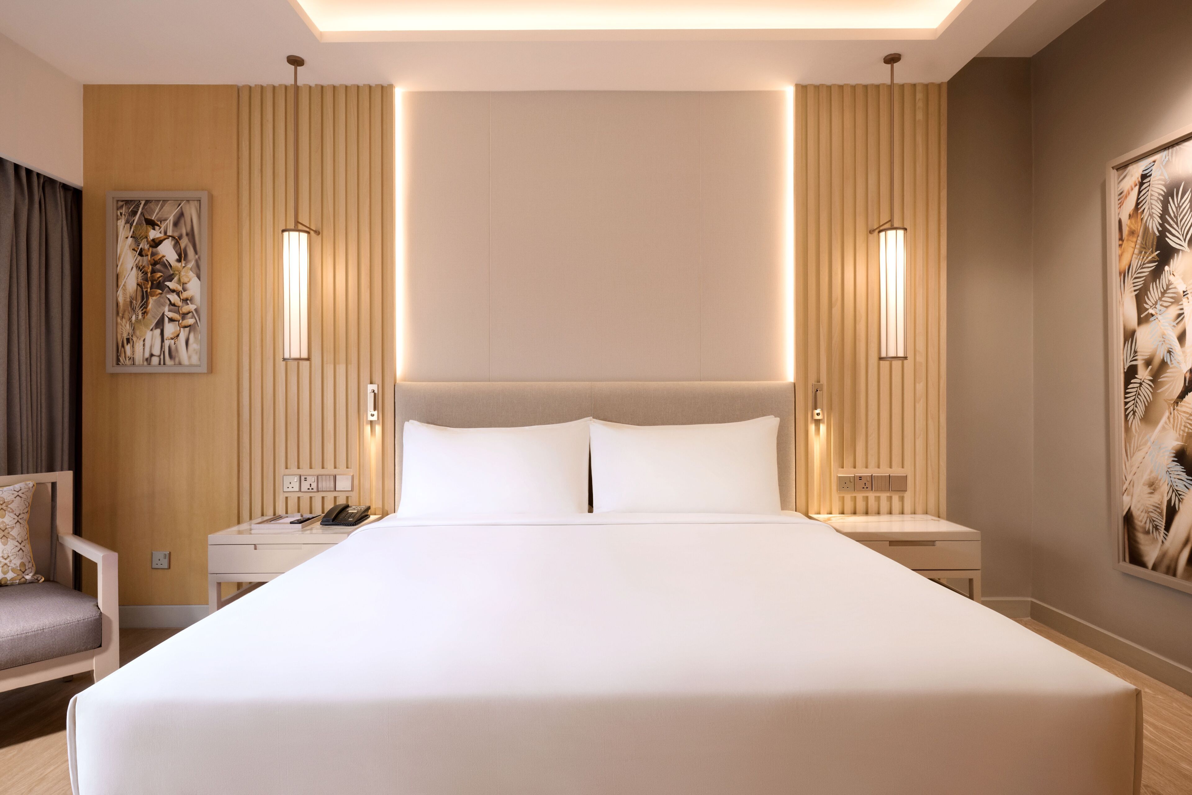 A hotel room with a large bed, bedside tables, a chair, and artwork on the walls.