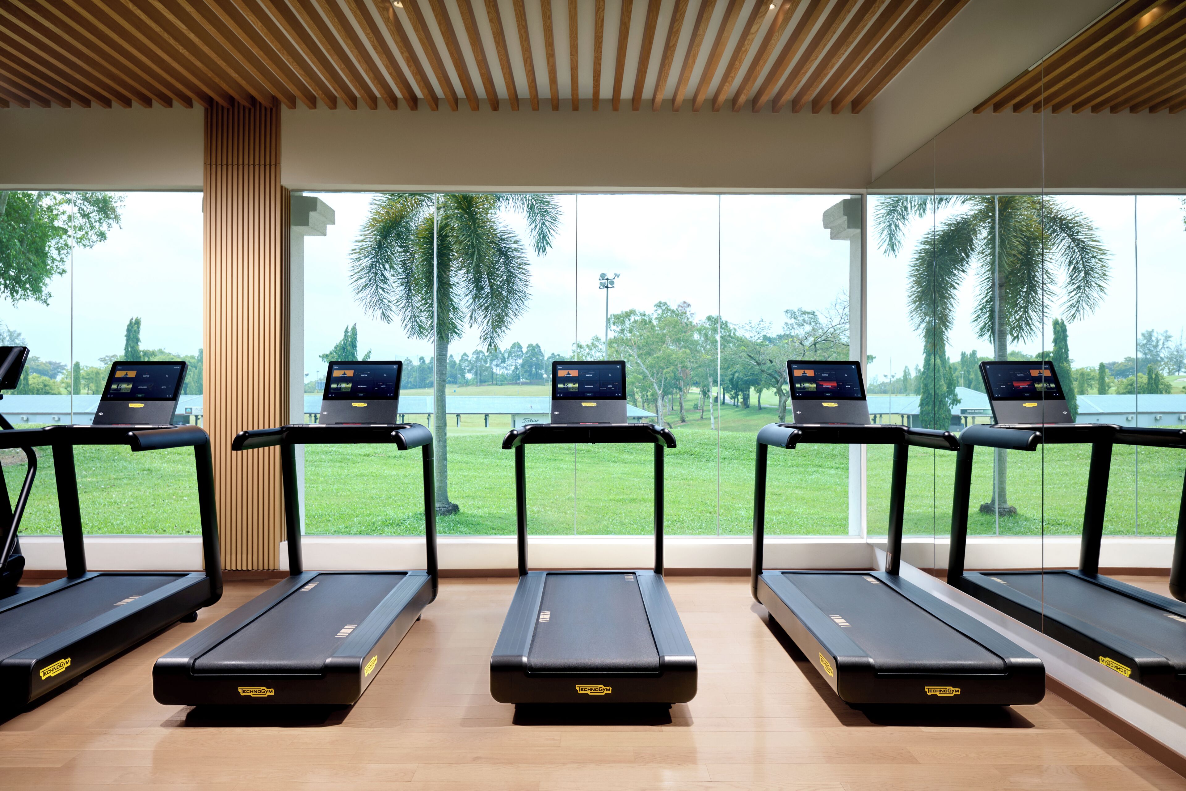 Una palestra con tapis roulant, ognuno dotato di schermo digitale, e ampie finestre che offrono vista su una zona verde esterna.