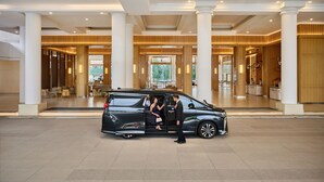 A black limousine parked in a spacious lobby with high ceilings, large columns, and a reception area.