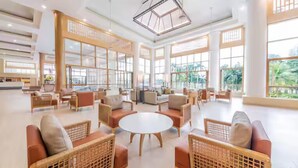 A spacious lobby with high ceilings, large windows, and a central round table surrounded by wicker furniture.