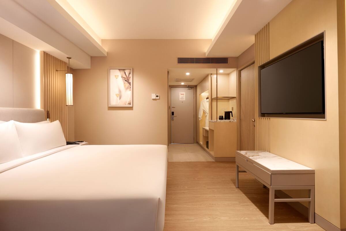 Une chambre d’hôtel comprenant un lit, une table de chevet, une télévision et une salle de bain avec un miroir et un lavabo.