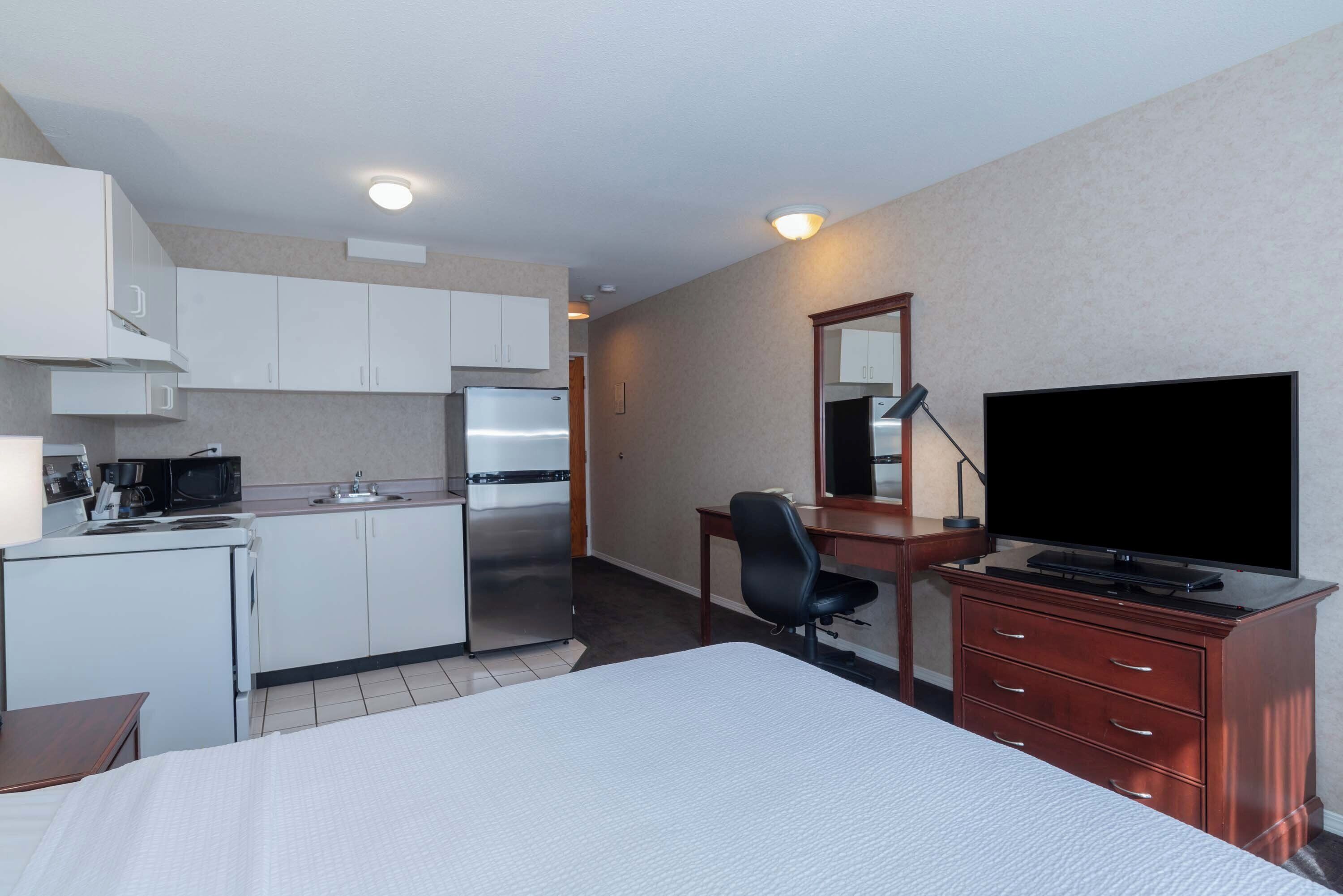 A hotel room with a bed, a desk, a chair, a TV, a dresser, a microwave, a refrigerator, and a kitchenette.