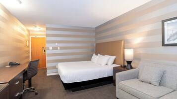 Ein Hotelzimmer mit einem Bett, einem Schreibtisch, einem Sessel, einer Couch und einem Nachttisch mit Lampe.