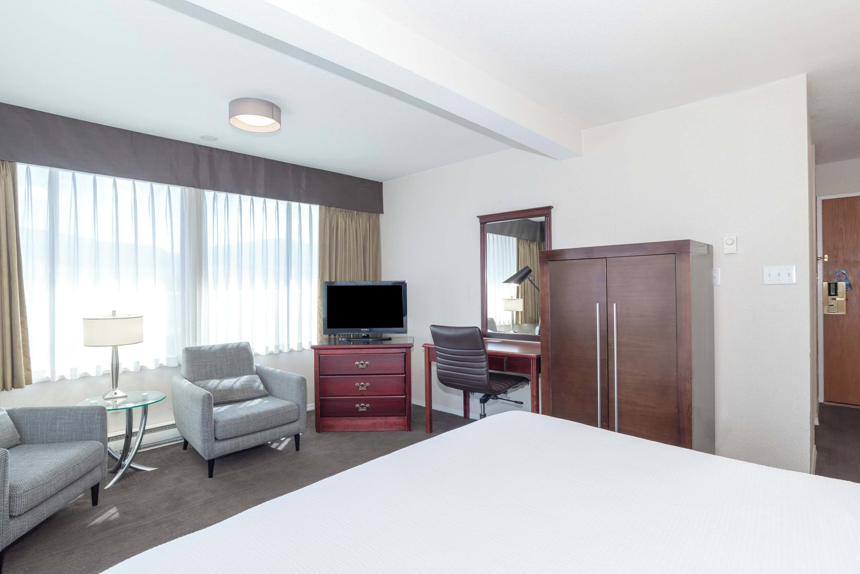 Una habitación de hotel con una cama grande, televisión, escritorio con silla, armario y lámpara.