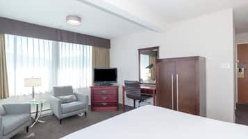 Una habitación de hotel con una cama grande, televisión, escritorio con silla, armario y lámpara.