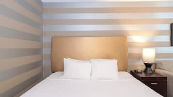 A neatly made bed with white linens and two pillows, a bedside table with a lamp, and a striped wall.