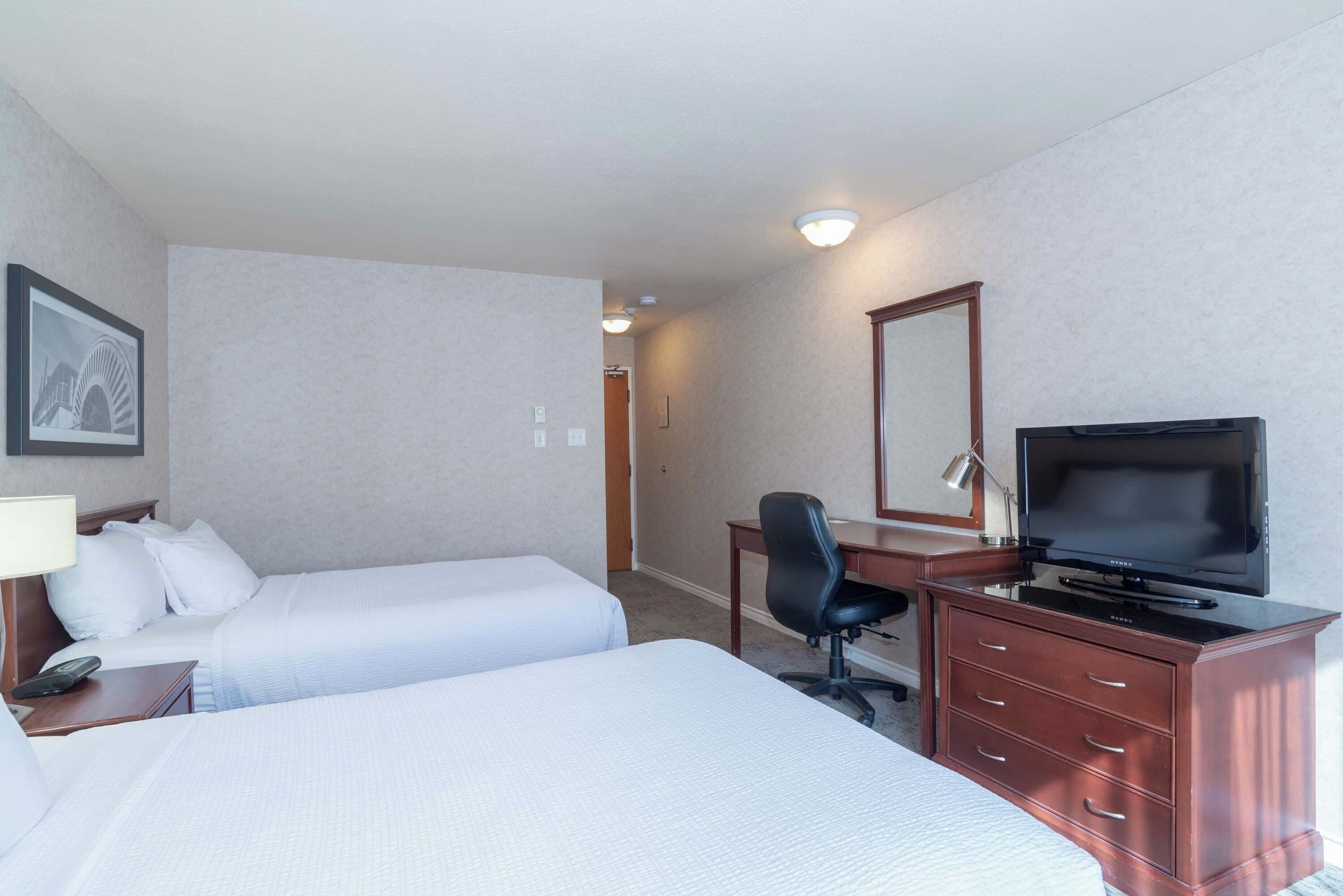 A hotel room with two beds, a desk with a TV, a chair, and a dresser.