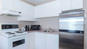 Una cocina moderna con armarios blancos, un refrigerador de acero inoxidable, un microondas, una estufa y una cafetera.