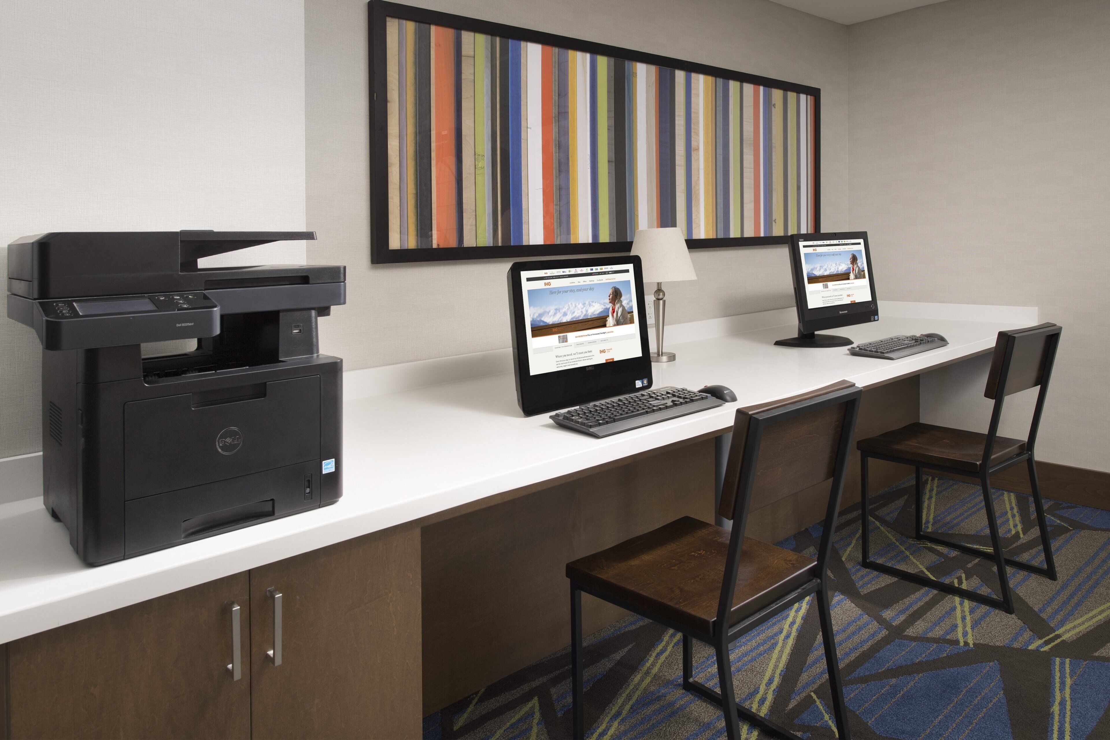 Een hotelwerkplek met een computer, een printer en twee stoelen.