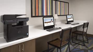 Un espacio de trabajo en un hotel, con una computadora de escritorio, una impresora y dos sillas.