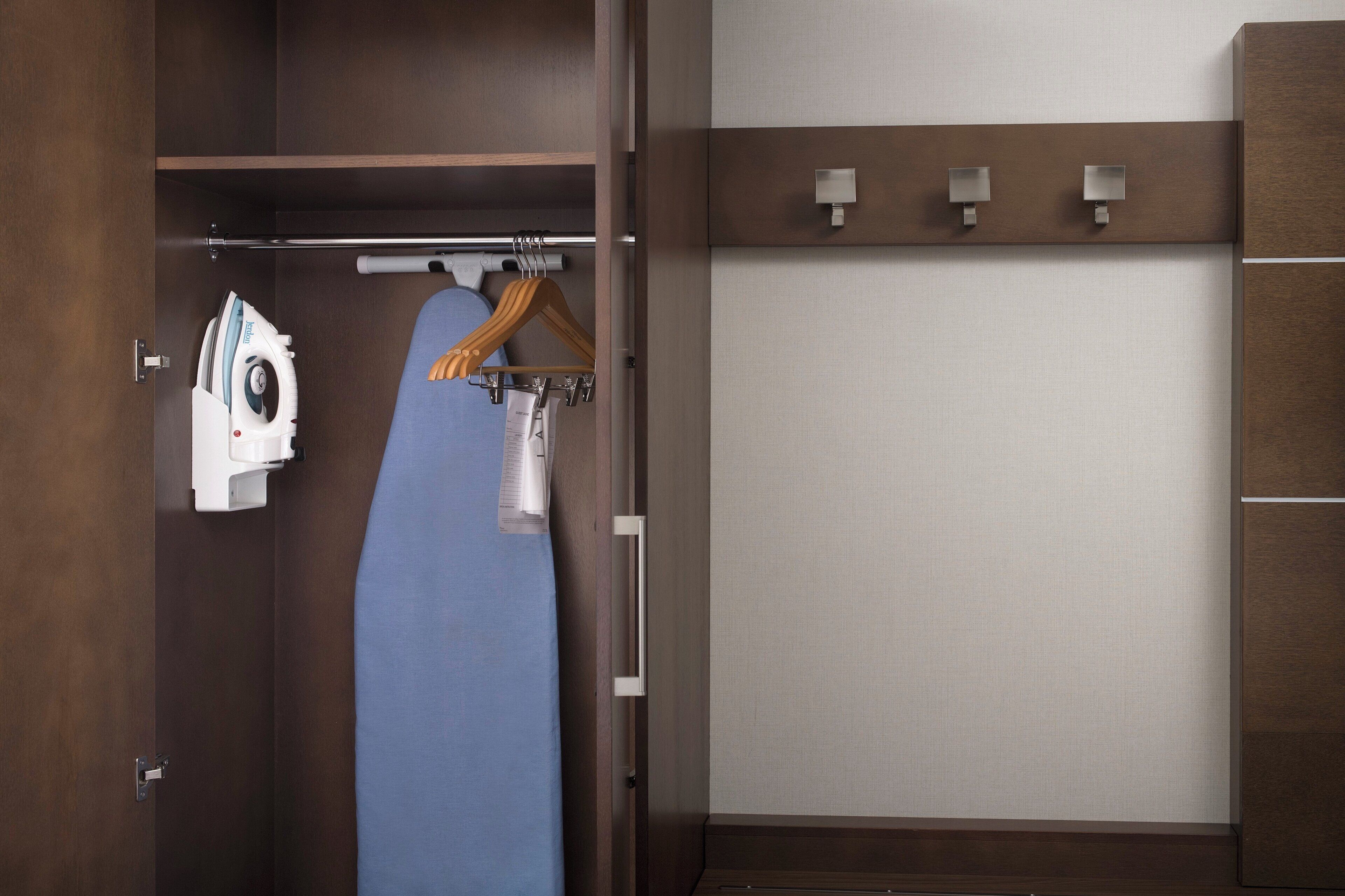 A hotel room with a wooden wardrobe, a hanging ironing board, and a wall-mounted light fixture.