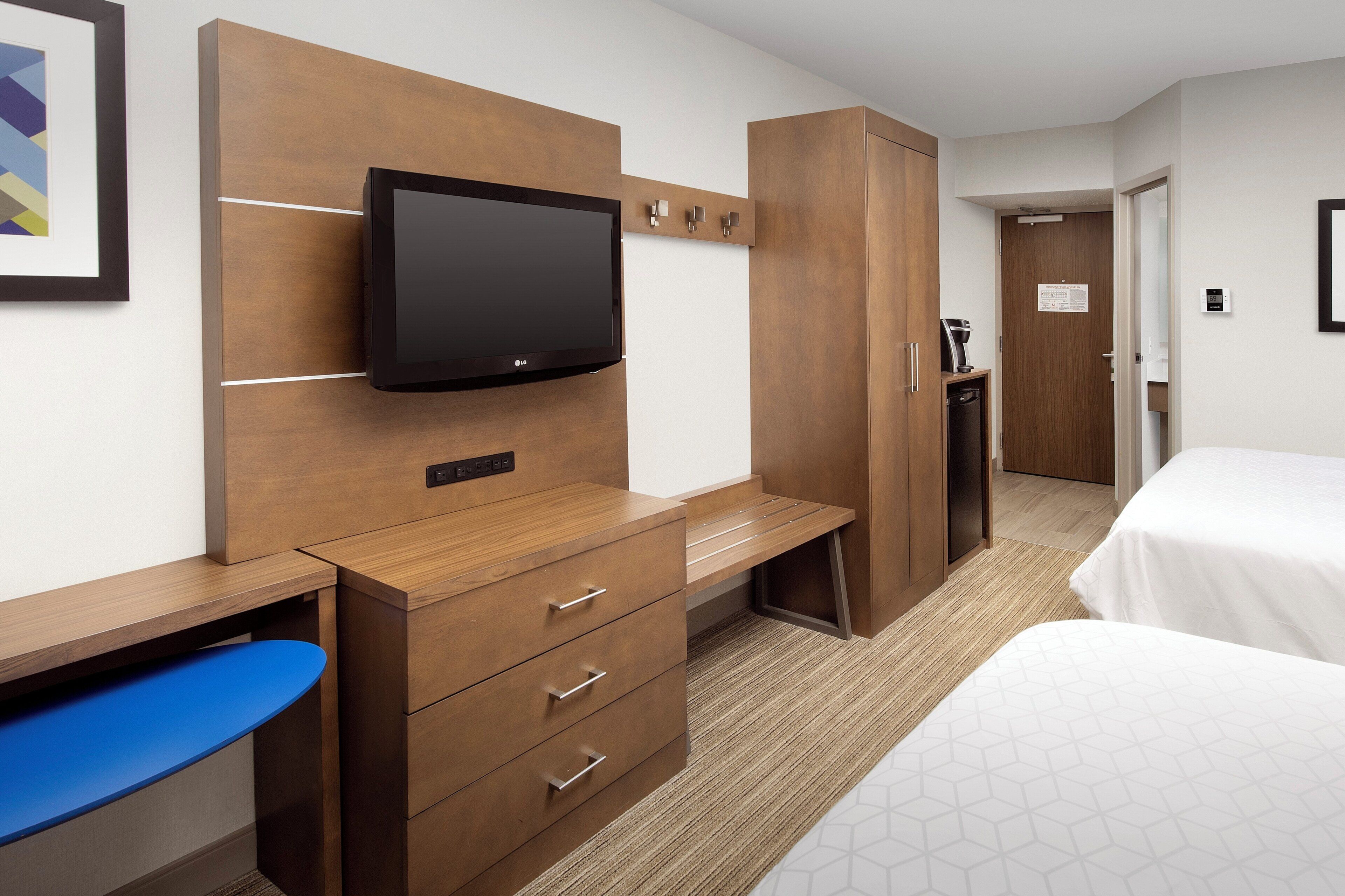 Una habitación de hotel con escritorio de madera, televisor de pantalla plana, cama y armario.
