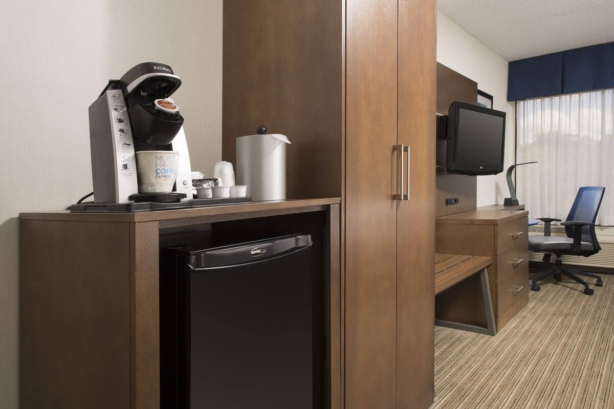 A hotel room with a coffee maker, a television, a desk, and a chair.