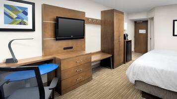 Una habitación de hotel con cama, escritorio, silla, televisor, armario y cafetera.