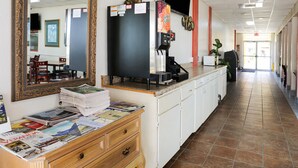 A hotel lobby with a reception desk, a coffee machine, a stack of newspapers, and a mirror.