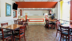 A restaurant interior with wooden tables and chairs, a counter with a menu, and a framed picture on the wall.