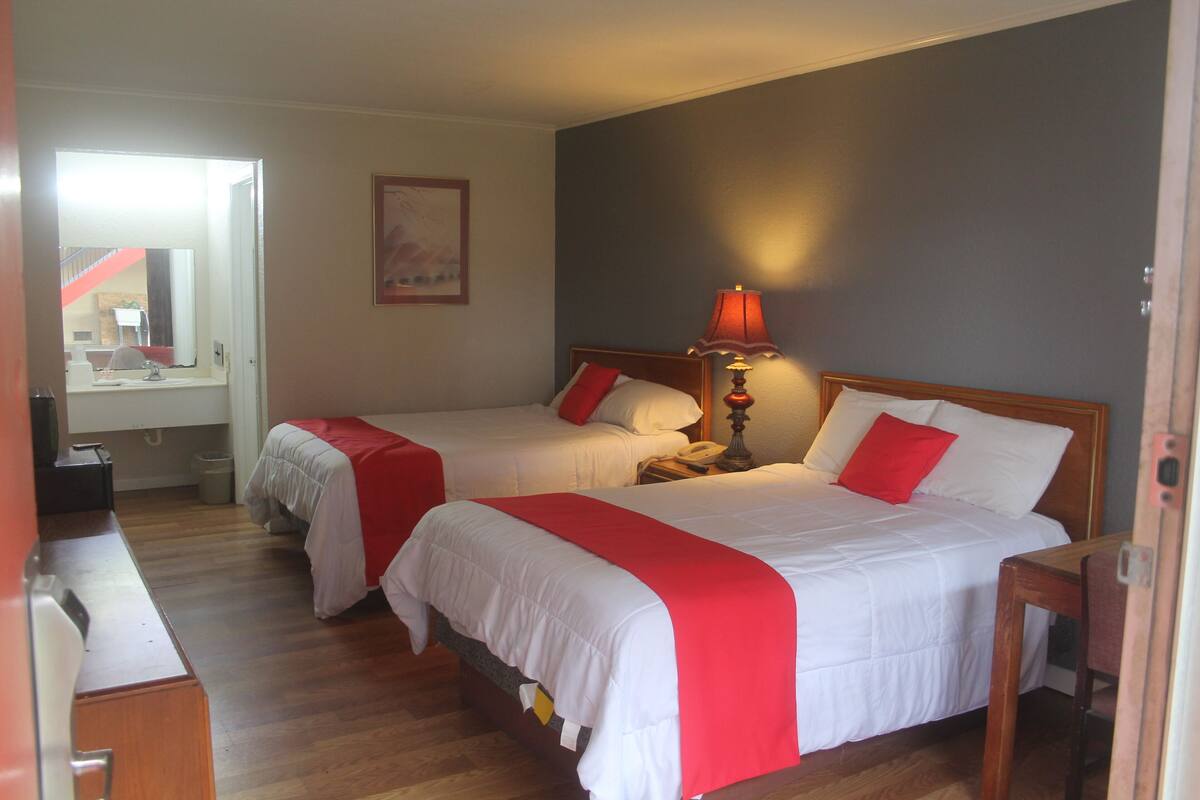 A hotel room with two beds, a desk, and a lamp.