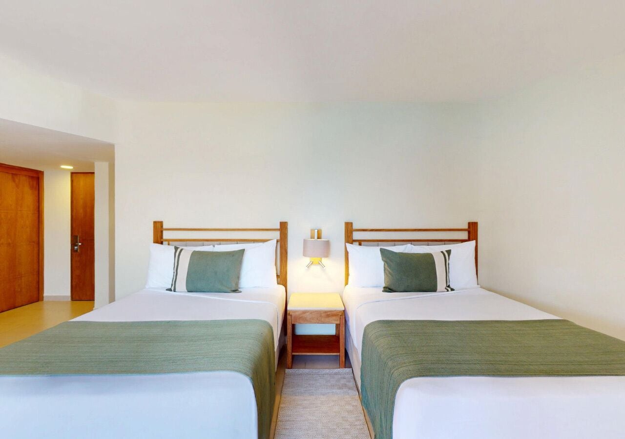 A hotel room with two single beds, a nightstand with a lamp, and a wooden door.