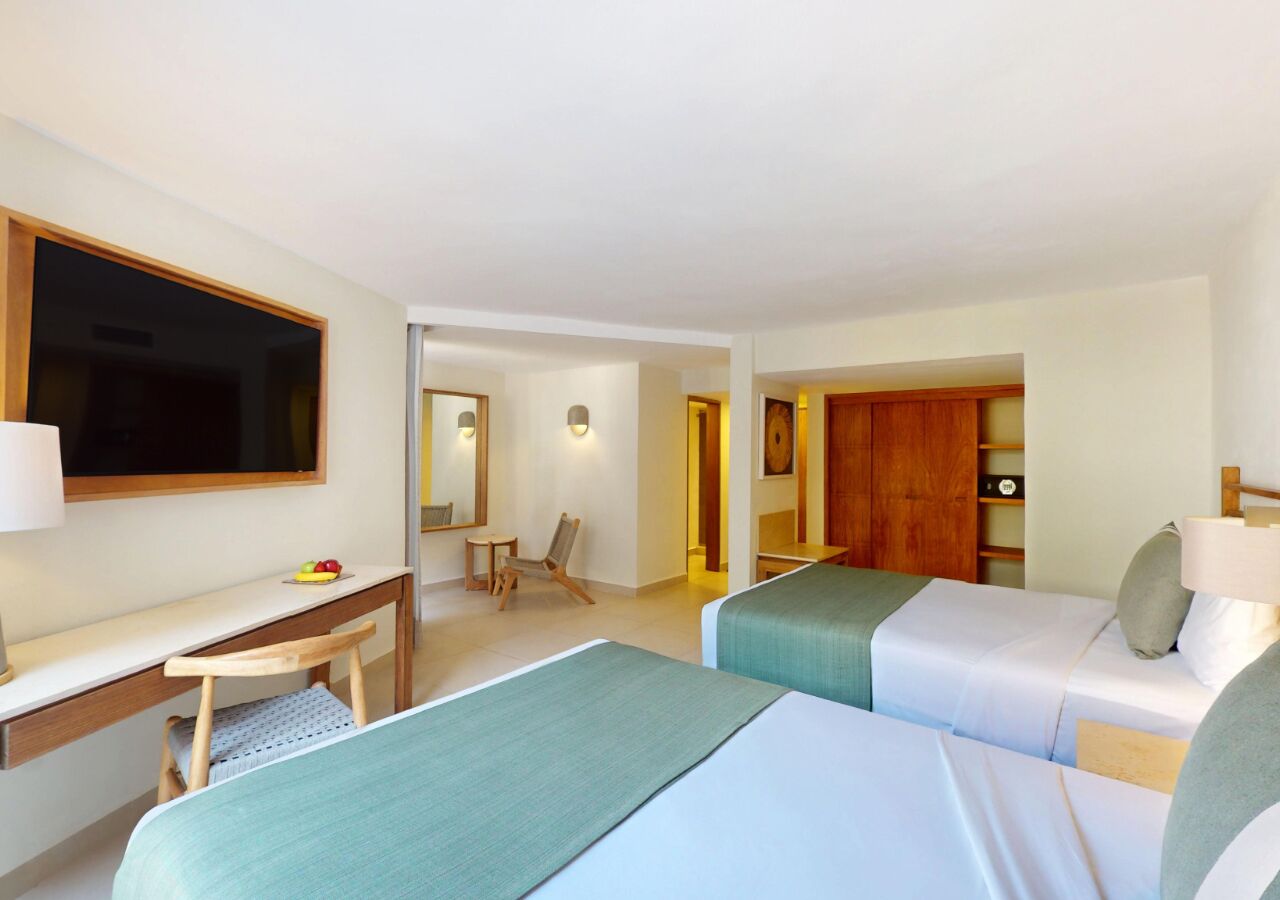 A hotel room with two beds, a desk, a chair, a TV, and a wardrobe.