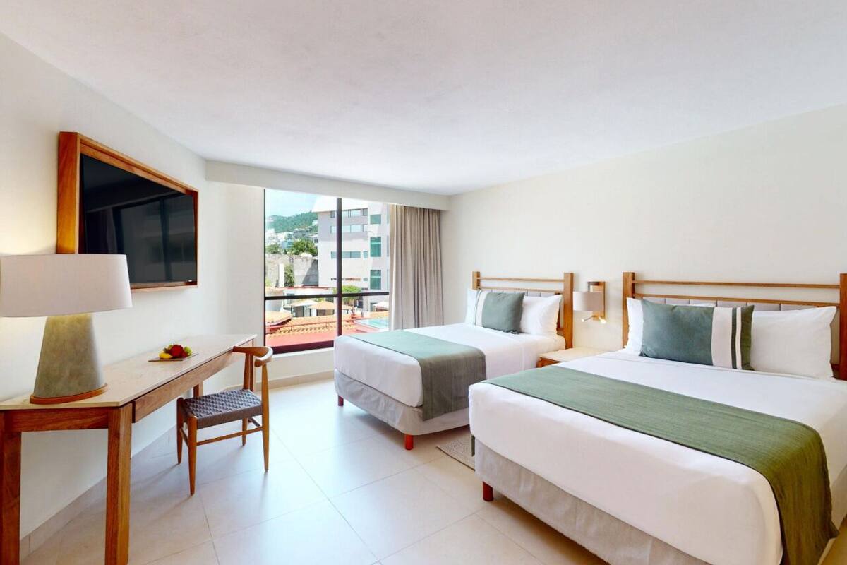 Quarto de hotel com duas camas, uma escrivaninha, uma cadeira e uma televisão.