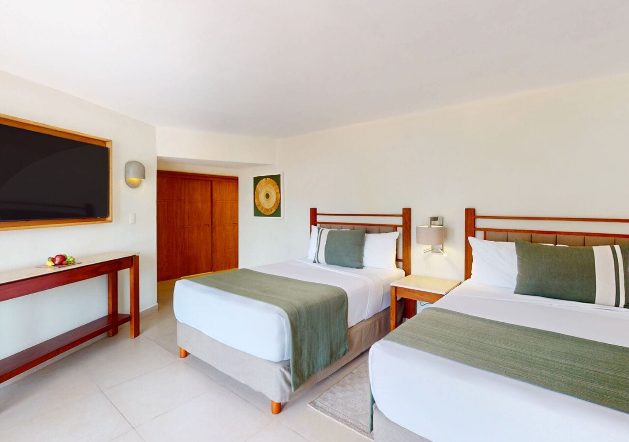 Habitación de hotel con dos camas, un televisor, un escritorio de madera y una puerta.