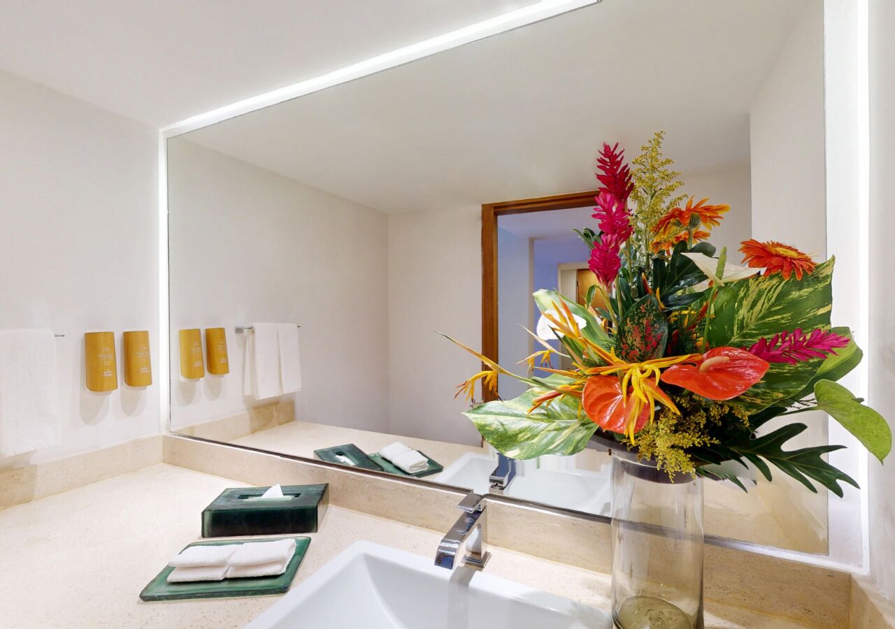 Ein Badezimmer mit großem Spiegel, zwei Waschbecken und einem Blumenstrauß.