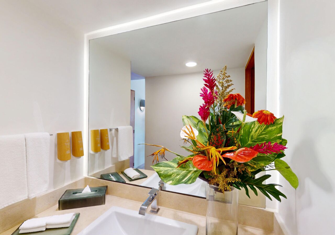 Une salle de bain avec un lavabo, un miroir et un vase de fleurs.