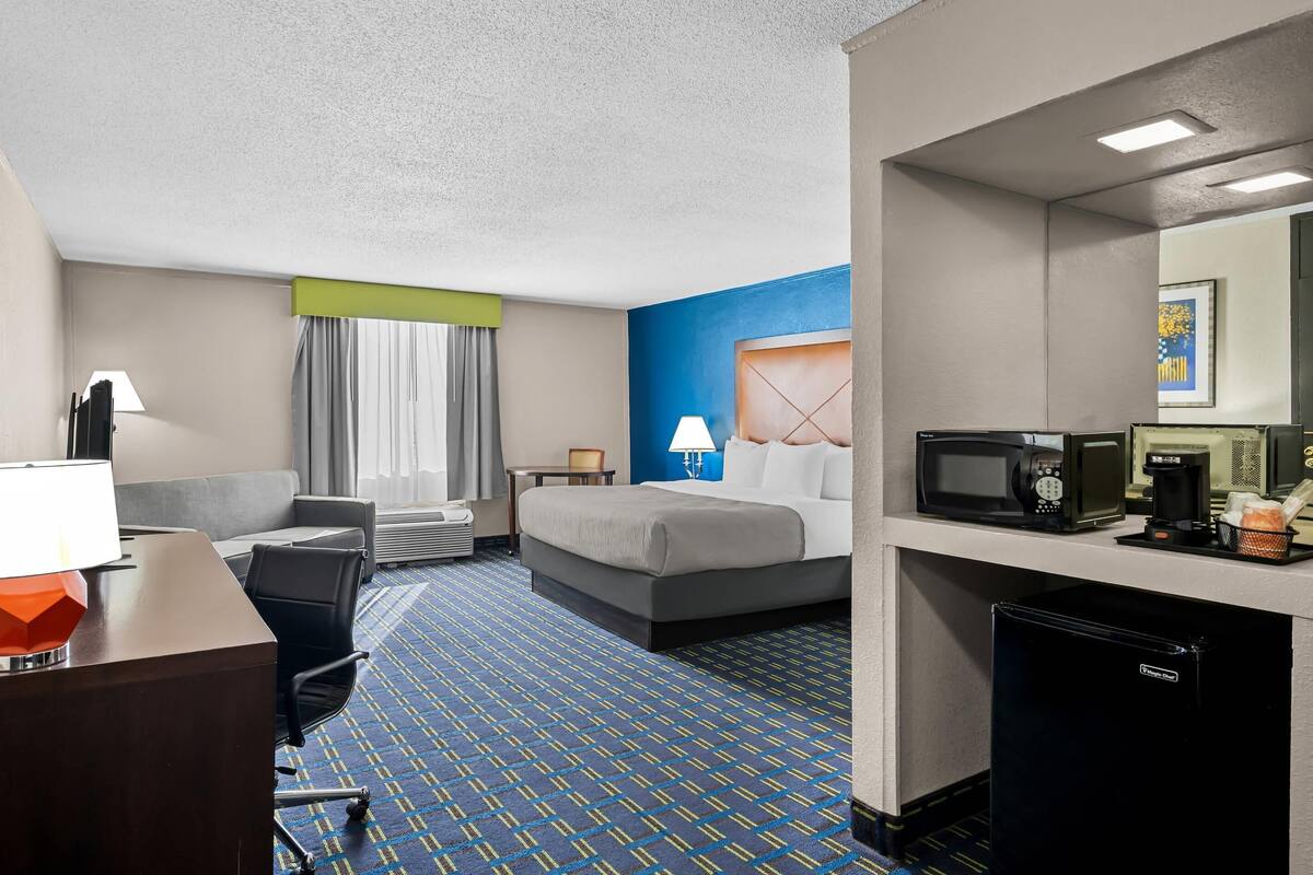 Una habitación de hotel con cama, escritorio, silla y kitchenette.