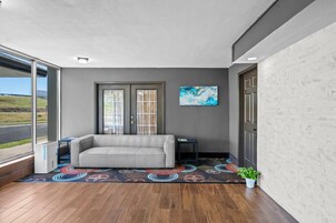 Una habitación moderna con un sofá gris, una alfombra colorida y un amplio ventanal con vistas al exterior.