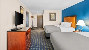 Ein Hotelzimmer mit zwei Betten, einem Fernseher, einem Schreibtisch und einer Lampe.