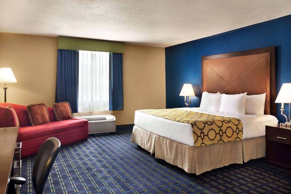 Habitación de hotel con una cama, un sofá rojo, un escritorio con silla y una ventana con cortinas.